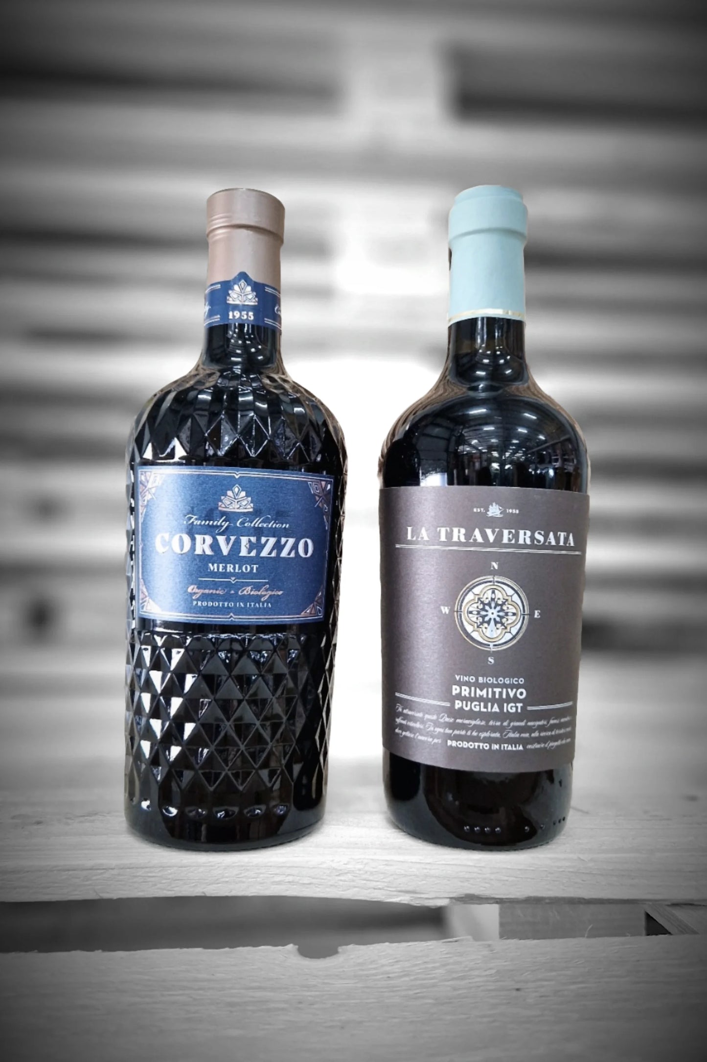 Drie flessen Corvezzo Merlot en drie Primitivo tegen vervaagde achtergrond – Mixdoos J (3× Merlot, 3× Primitivo)