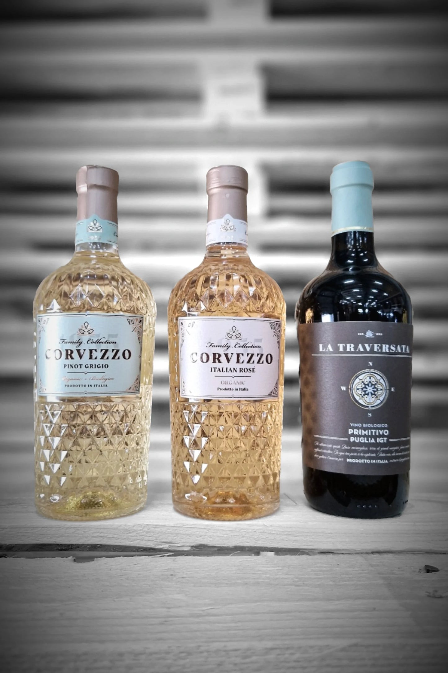 Twee flessen Corvezzo Pinot Grigio, twee Rosé en twee Primitivo tegen vervaagde achtergrond – Mixdoos N (2× PG, 2× Rosé, 2× Primitivo)