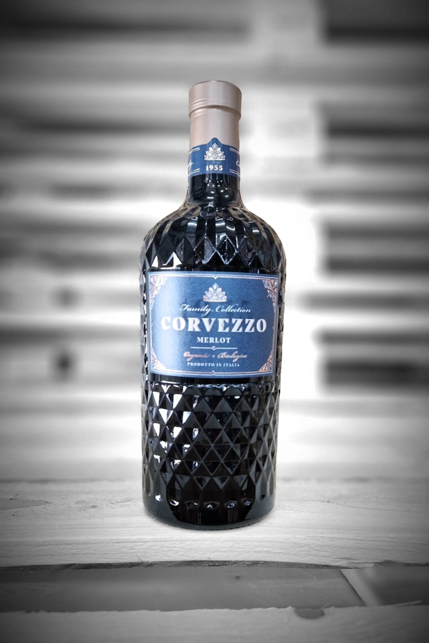 Fles Corvezzo Merlot tegen vervaagde loodsachtergrond – Mixdoos C (6× Merlot)